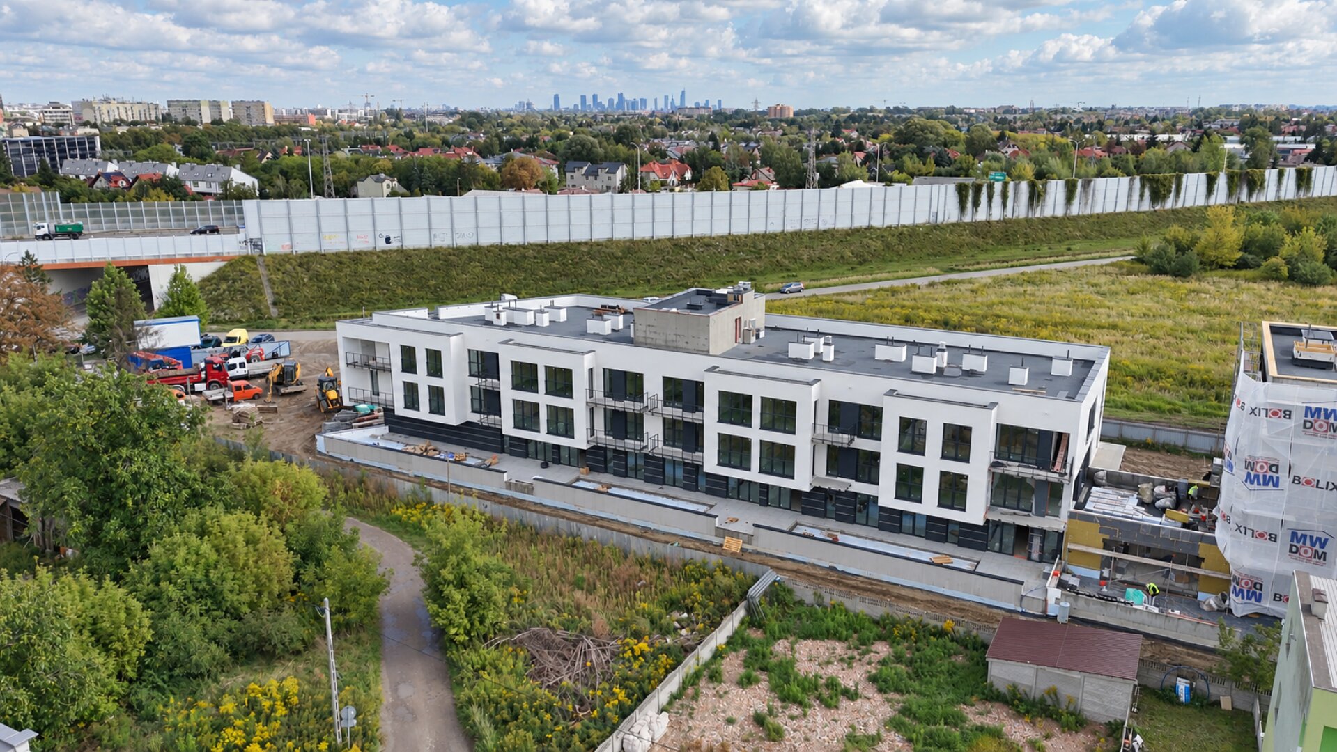 Miniatura: Budynek A z gotą białą elewacją — widok z drona z panoramą Warszawy w tle